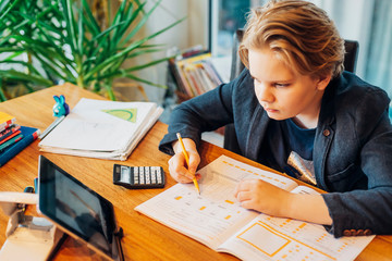 Boy sitting at desk with workbook and tablet