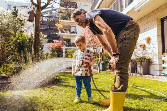 Father And Son Watering The Lawn In Garden