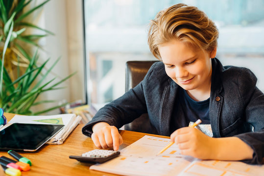 Smiling boy sitting at desk with workbook and pocket calculator