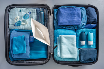 Overhead view of packed suitcase with clothes, swimming goggles and paper boat