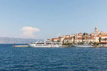 Fototapeta na wymiar Korcula island with the old city walls, view from the sea on a sunny day in the summer blue sky. Clear adriactic sea and cruise ships docked at harbor. The south mediterranean coast of Croatia, Europe