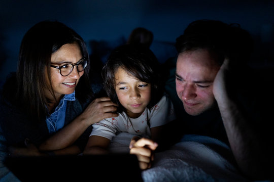 Parents and son lying together on bed at home using digital tablet