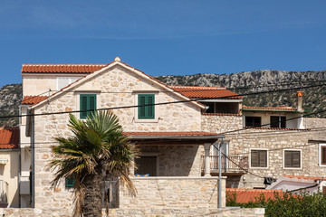 Fototapeta na wymiar A detail of a mediterranean house with a typical orange roof, a light facade with a rustic stone structure and a palm tree on a sunny day in summer and a clear blue sky in Dalmatia Croatia