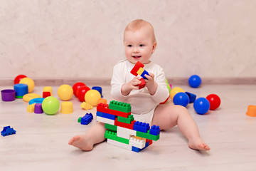little baby in white clothes sits and plays with a multi-colored designer at home, child development