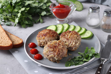 Beef cutlets served with cucumber and tomato sauce on a gray plate on gray concrete background, Closeup, Horizontal format