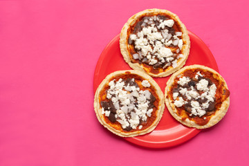 Mexican red sopes with cheese and beans on pink background