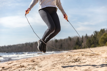 The girl is engaged in sports in nature. exercise with rope, sand and lake.