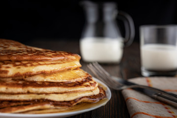Breakfast, golden pancakes folded on a gray plate, fork and knife on wooden boards in the background, milk in a decanter and a glass, rustic style, dim light, shallow depth of field, selective focus.