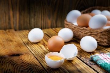 Farm eggs white and brown lie on a wooden table and in a basket, close-up, low light, selective focus, shallow depth of field. Organic food concept
