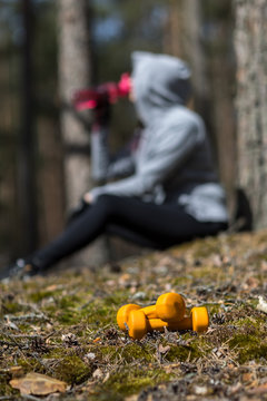 The girl rests after playing sports. Dumbels close-up and a bottle of water in hand. Exercise charging in nature.