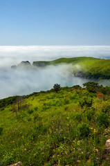 Fototapeta premium Sea lagoon in the fog surrounded by steep shores and green hills. View from above.
