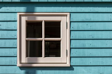 Naklejka na ściany i meble A small window of a tiny house with a white frame and light blue colored hard wooden facade consisting out of panels on a sunny day. Horizontal shot