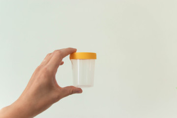 Hand holding empty urine plastic container on white background