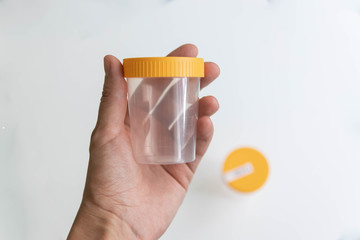 Hand holding empty urine plastic container on white background