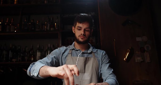 Professional bartender masterly creating a cocktail in modern bar. Experienced barman mixing red alchoholic beverage before serving - food and drink, nightlife close up 4k footage