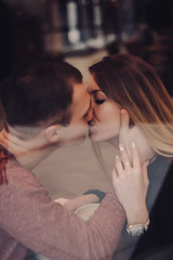 Fototapeta premium Cute brunette loving couple in cozy warm sweaters on a date at the cafe looking at the phone, using it. cold autumn, winter or spring day, european city. indoors
