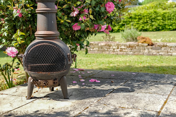  Rusty wood burning patio heater on paving slabs in front of a camelia bush on a sunny day