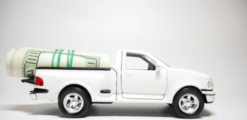 Car and money. White Car (pickup) with twisted hundred-dollar bills in the trunk. on a gray background. Buying a car / Trade deal. Closeup. Finance concept.