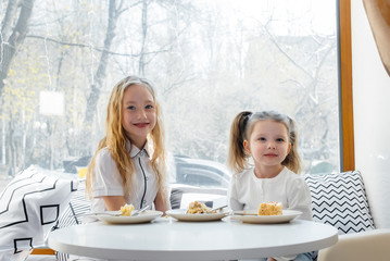 Two cute little girls are sitting in a cafe and playing on a Sunny day. Recreation and lifestyle.