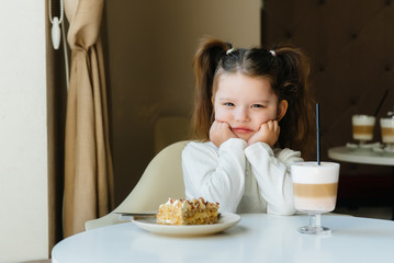 A cute little girl is sitting in a cafe and looking at a cake and cocoa close-up. Diet and proper nutrition