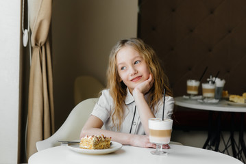 A cute little girl is sitting in a cafe and looking at a cake and cocoa close-up. Diet and proper nutrition