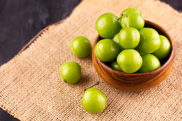 Unripe green plums on a black wooden table