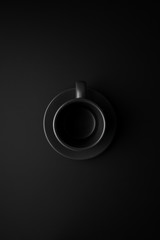 Empty black cup and saucer on a black surface in the center of the frame. Flat lay.