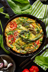 Vegetarian Frittata with the addition of green asparagus, green peas, spinach and cherry tomatoes in a cast iron skillet top view