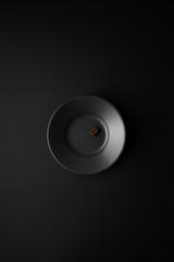 One coffee bean in black saucer on a black surface in the center of the frame. Flat lay.