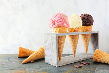 Ice creme cone table scene with rustic wood holder against a marble background. Strawberry, vanilla...