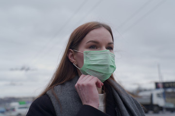 Beautiful young girl went outside in a medical mask on a background of gray sky.