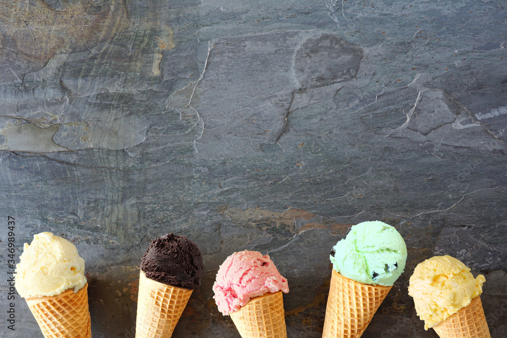 Poster ice cream cone bottom border with a variety of flavors. top view over a dark slate stone background.