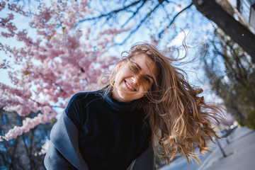 Sakura branches with flowers on a tree on the city streets. Happy woman girl spinning on the street with blooming sakura. Gorgeous fashionable girl outdoors. Sakura tree blossoms.