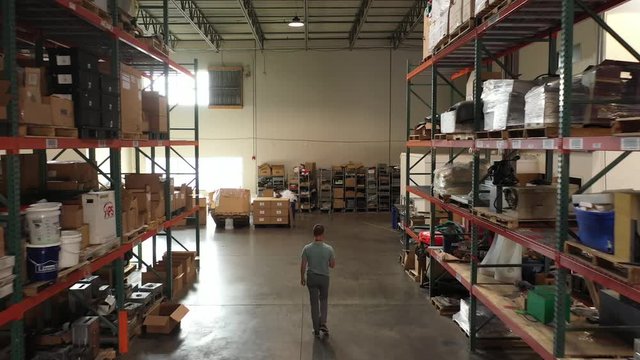 Aerial of worker walking down row of warehouse shelves