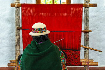 A senior indigenous Bolivian Aymara woman in traditional clothing doing a demonstration of fabric...