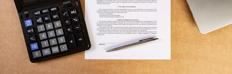 Flat lay of contract with laptop, pen and calculator on the table.