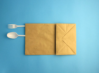 white plastic spoon and fork in a paper bag on a blue background, ecology concept