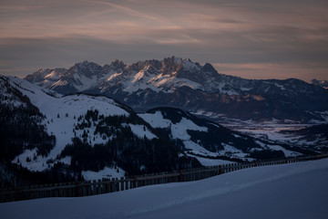 Fototapeta premium Mountains of mountain range Wilder Kaiser at Fieberbrunn during sunset in winter with snow, forest and valley, clouds in the sky, Tyrol Austria.