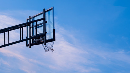 Low angle and rear side view of outdoor transparent basketball backboard against white cloud and blue sky background