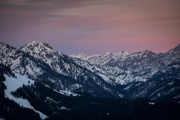 Fototapeta na wymiar Mountains of mountain range Wilder Kaiser at Fieberbrunn during sunset in winter with snow, forest and valley, clouds in the sky, Tyrol Austria.