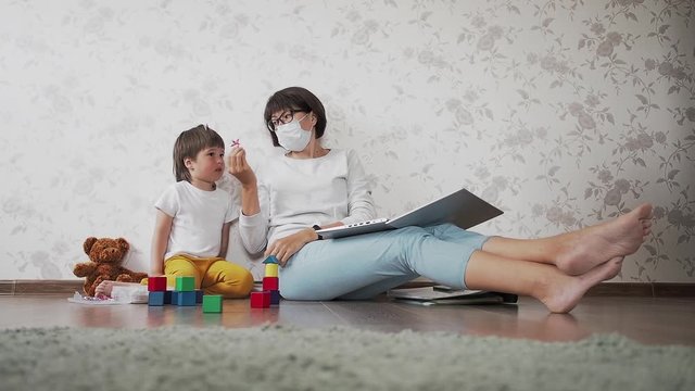 Mom and son sit at home quarantine because of coronavirus COVID19. Mother works remotely with laptop, son plays with toy blocks. Self isolation at home.