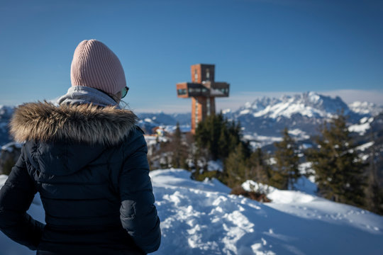 Woman at mountain Buchensteinwand at Wilder Kaiser with viewpoint and sightseeing spot Jakobskreuz in winter with snow, blue sky and sun, Fieberbrunn Tyrol Austria.