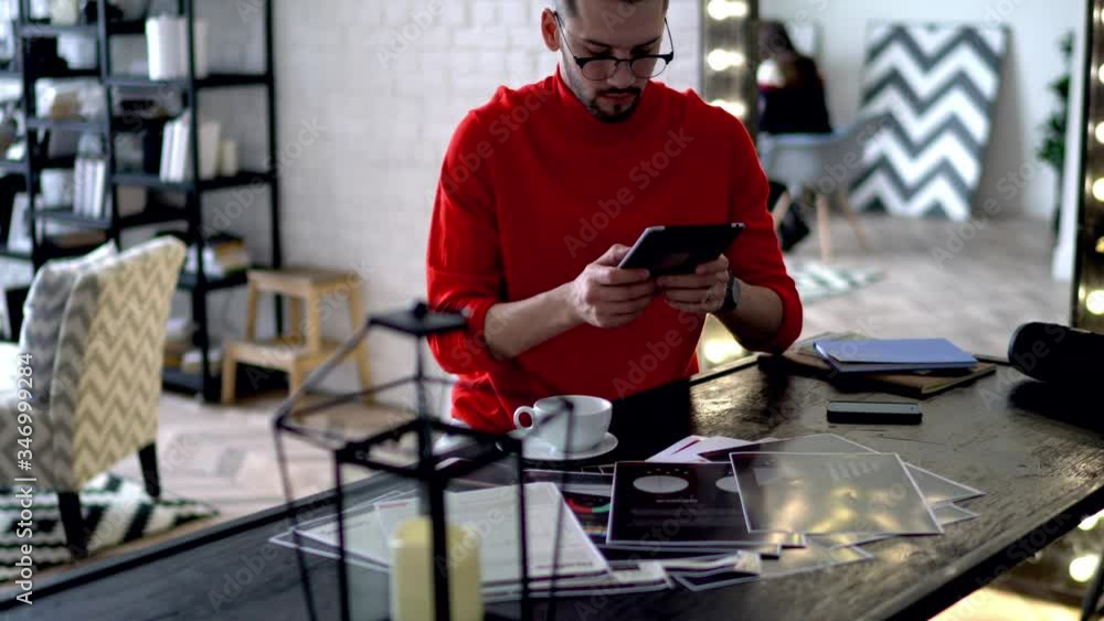 Poster young man in casual wear working at home using sketches and modern device for searching information 
