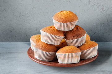 Many delicious fresh muffins are stacked in a pyramid on a ceramic plate. Sweet dessert.