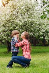 Fototapeta premium Mother and baby in blooming garden. Mom and child in spring. Springtime family scene. Flowers of apple or cherry tree.