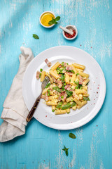 Italian recipe Pasta tortilloni with green pea, mint leaves, cheece, smoked bacon and cheese. Top view, blue background.