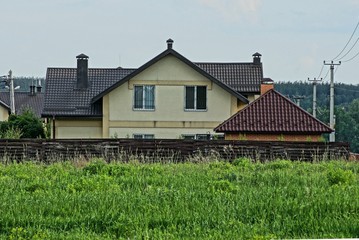 Fototapeta na wymiar private house with windows under a brown tiled roof behind a wooden fence in green grass