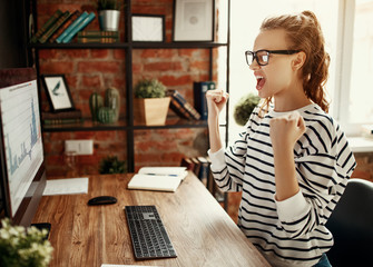 Excited woman celebrating victory while working at computer in loft office.