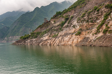 Shengli Street, China - May 6, 2010: Xiling gorge on Yangtze River. Rocky cliff above green water with navigation sign tower and descending cloudscape over green covered mountains.
