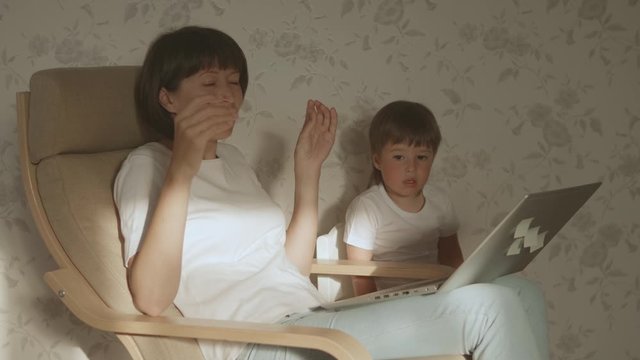 Mother and her toddler boy sit together on chair with laptop. Woman tries to remote work, but kid is asking for game or cartoons. quarantine lockdown because of coronavirus COVID-19. 10bit V-logL